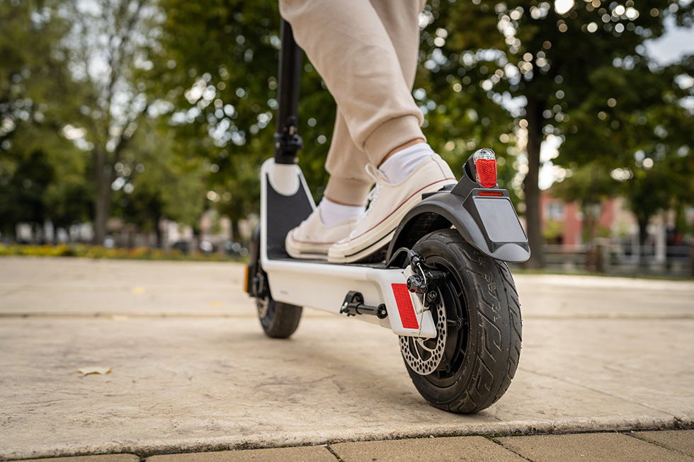 Feet of unknown man standing by or driving electric kick scooter e-scooter on the pavement in day eco friendly modern transport